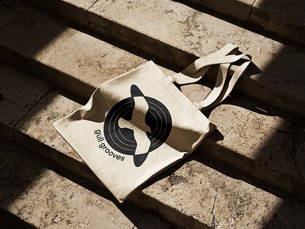 The logo printed on a canvas tote lying on sunlit stone steps.