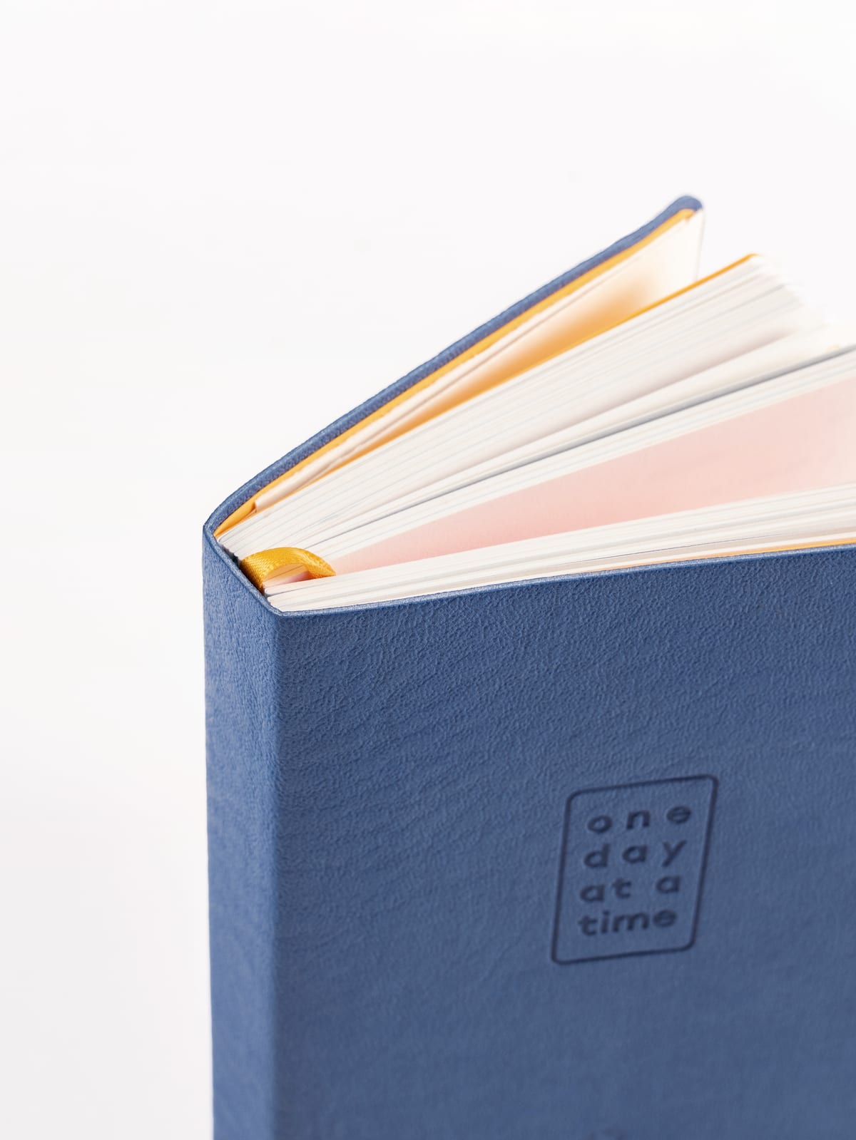 A close-up of the colored page edges, cream and peach blocks fanning open above the yellow ribbon and the debossed cover.