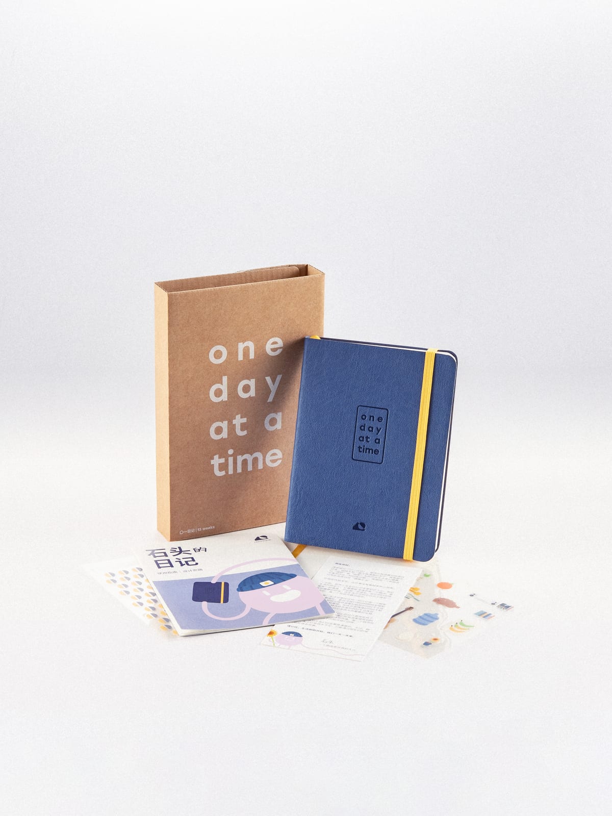 The journal leaning against its kraft box, the pamphlet and sticker sheets laid out in front.